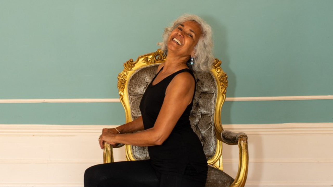 A woman tilts her head back and smiles while doing a ballet pose