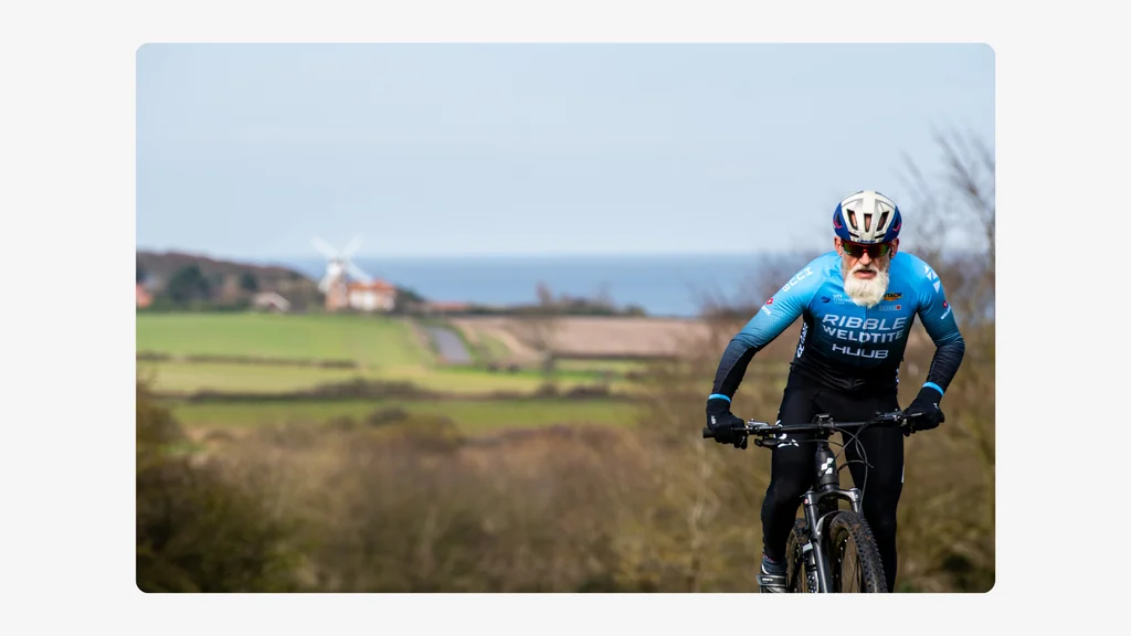 An older man rides a bike with landscape behind him. Credit: Darren Neale.