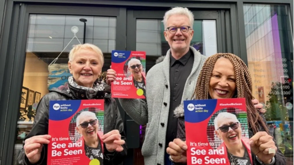 Three people outside a theatre holding Age Without Limits 'See and Be Seen' posters.