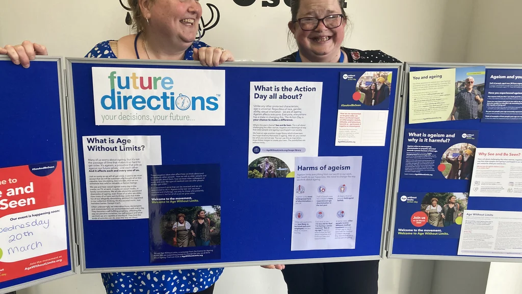 Two women hold up a display board which features the Future Directions logo and Age Without Limits Action Day materials.