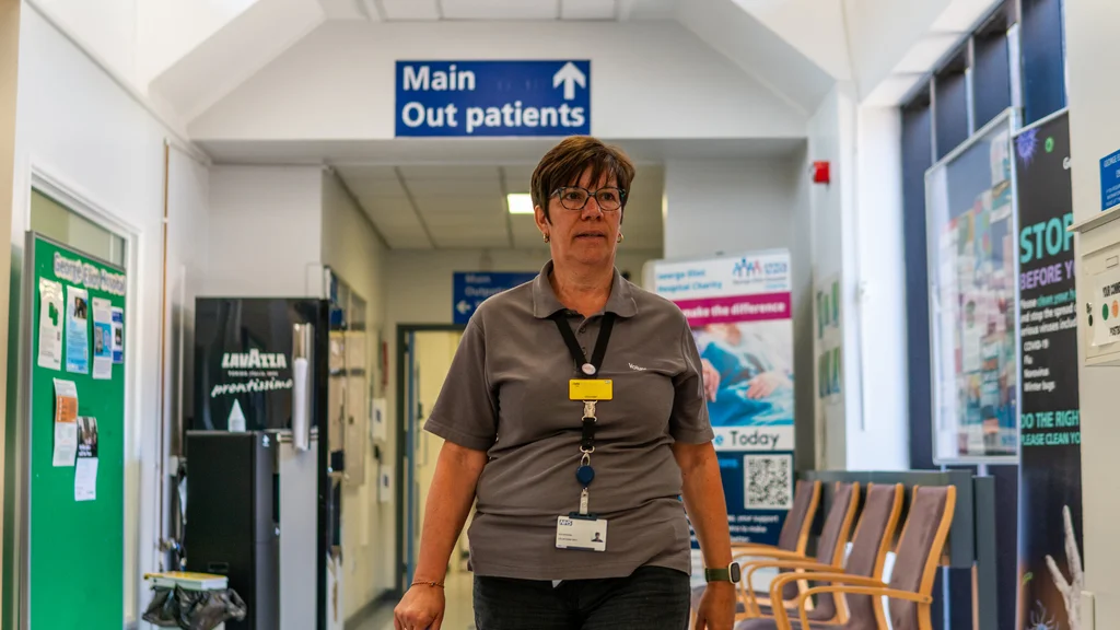 A woman volunteering in a hospital walks along a corridor