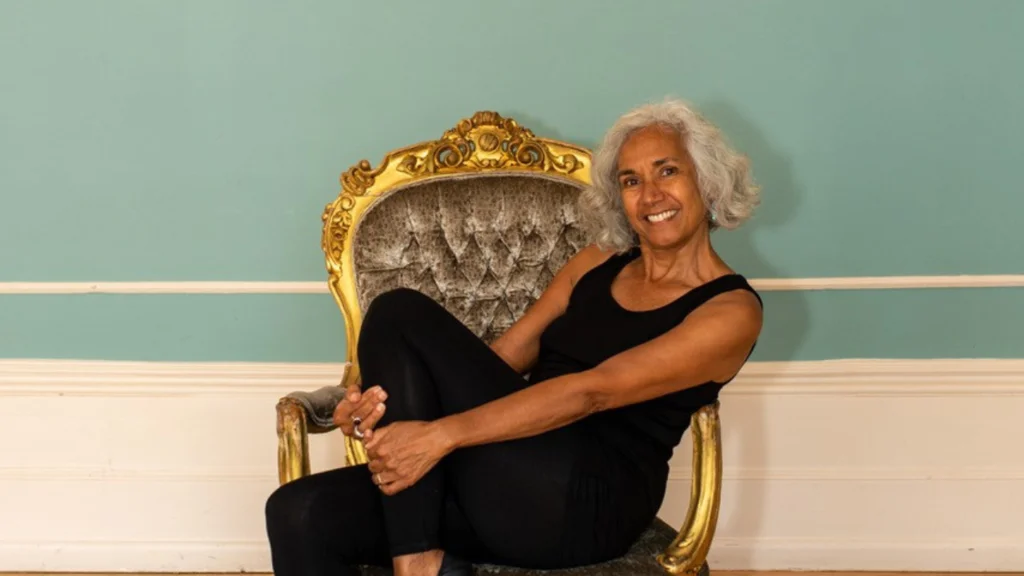 A woman with silver grey hair smiles and holds her leg up by her shin.