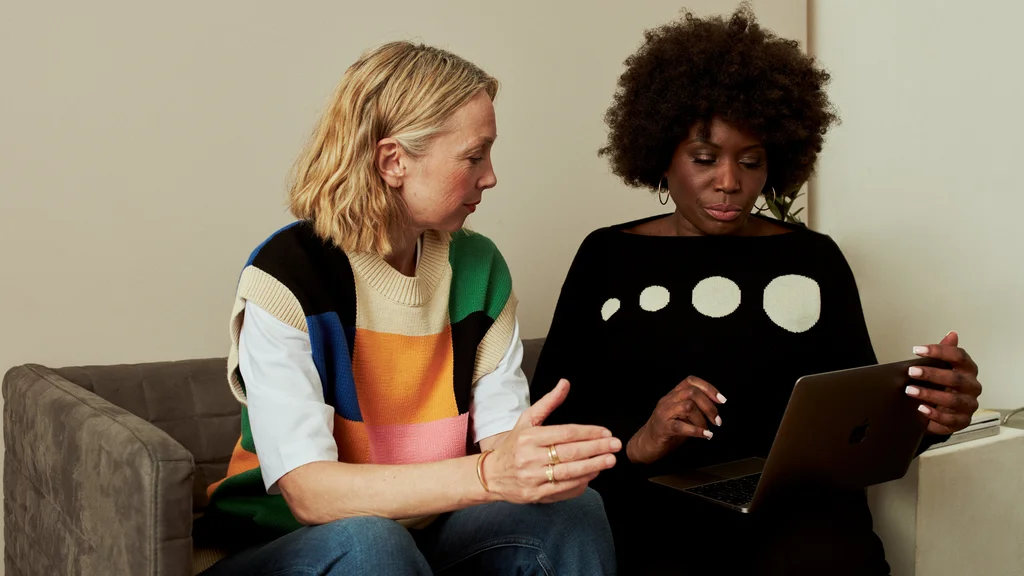 Two women sit on a sofa and look at an ipad screen