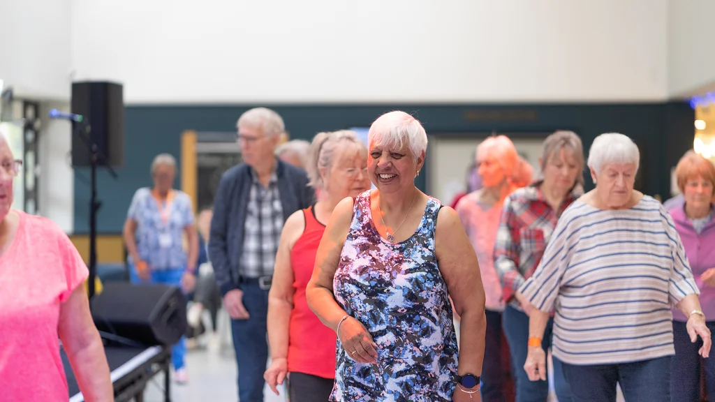 A group of people are doing an exercise class and a woman at the front of the group smiles