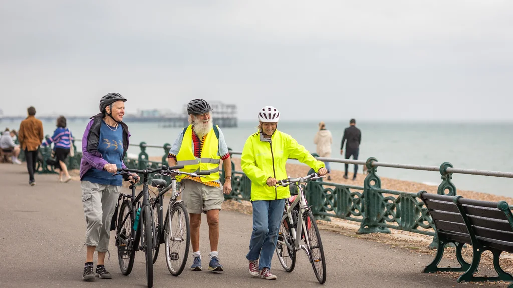 Three people walking along a seafront with bikes