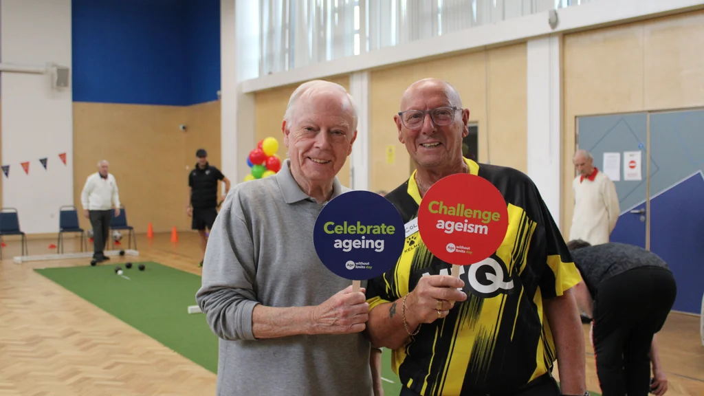 Two older men at Watford FC's Age Without Limits Day event holding up signs that say celebrate ageing and challenge ageism.